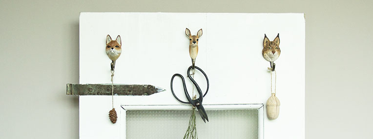 Hooks with hand carved animal sculptures shaped like a lynx, fox and a deer hanging on a door